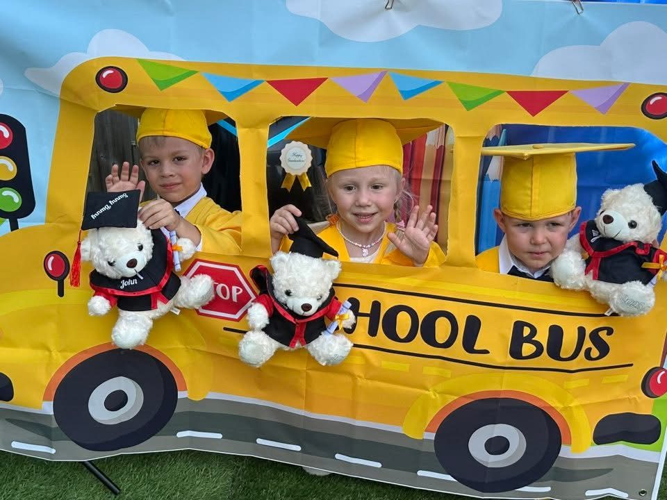Children in a school bus photo prop with graduation bears